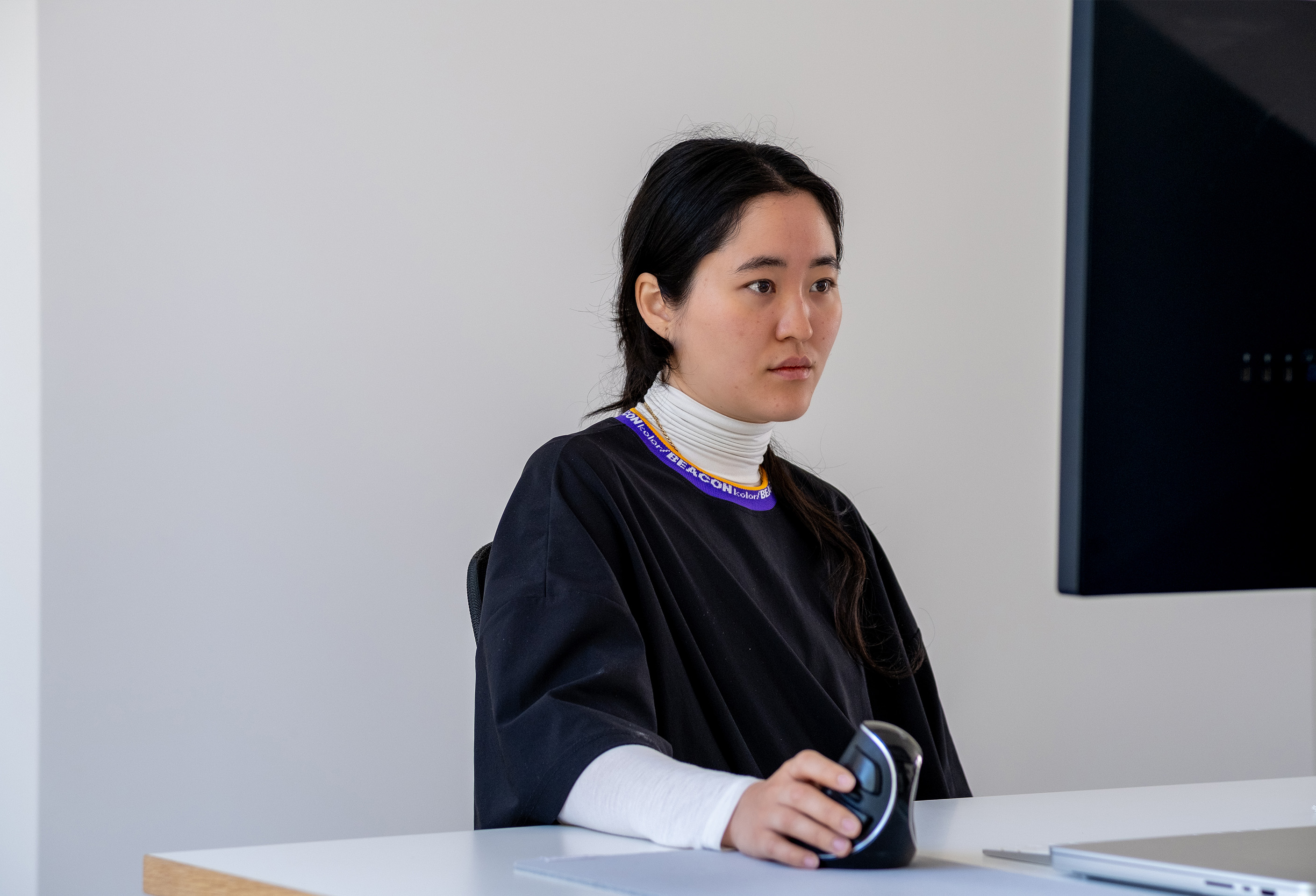 Joanne at her desk, holding an ergonomic mouse and looking to the side in focused concentration, curating design memes