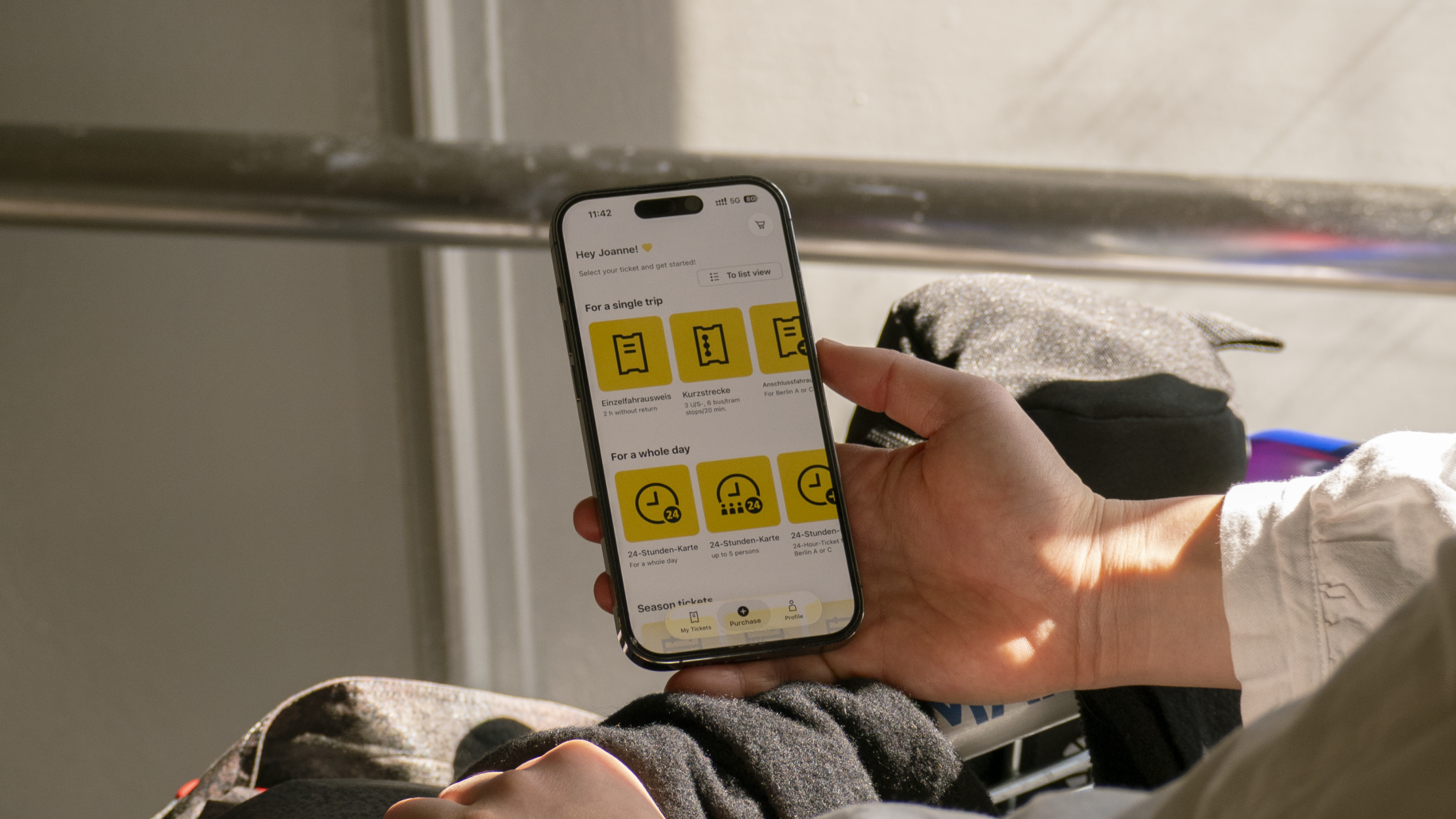 Hand holding an iPhone, showing the app's home screen with yellow category tiles for ticket options