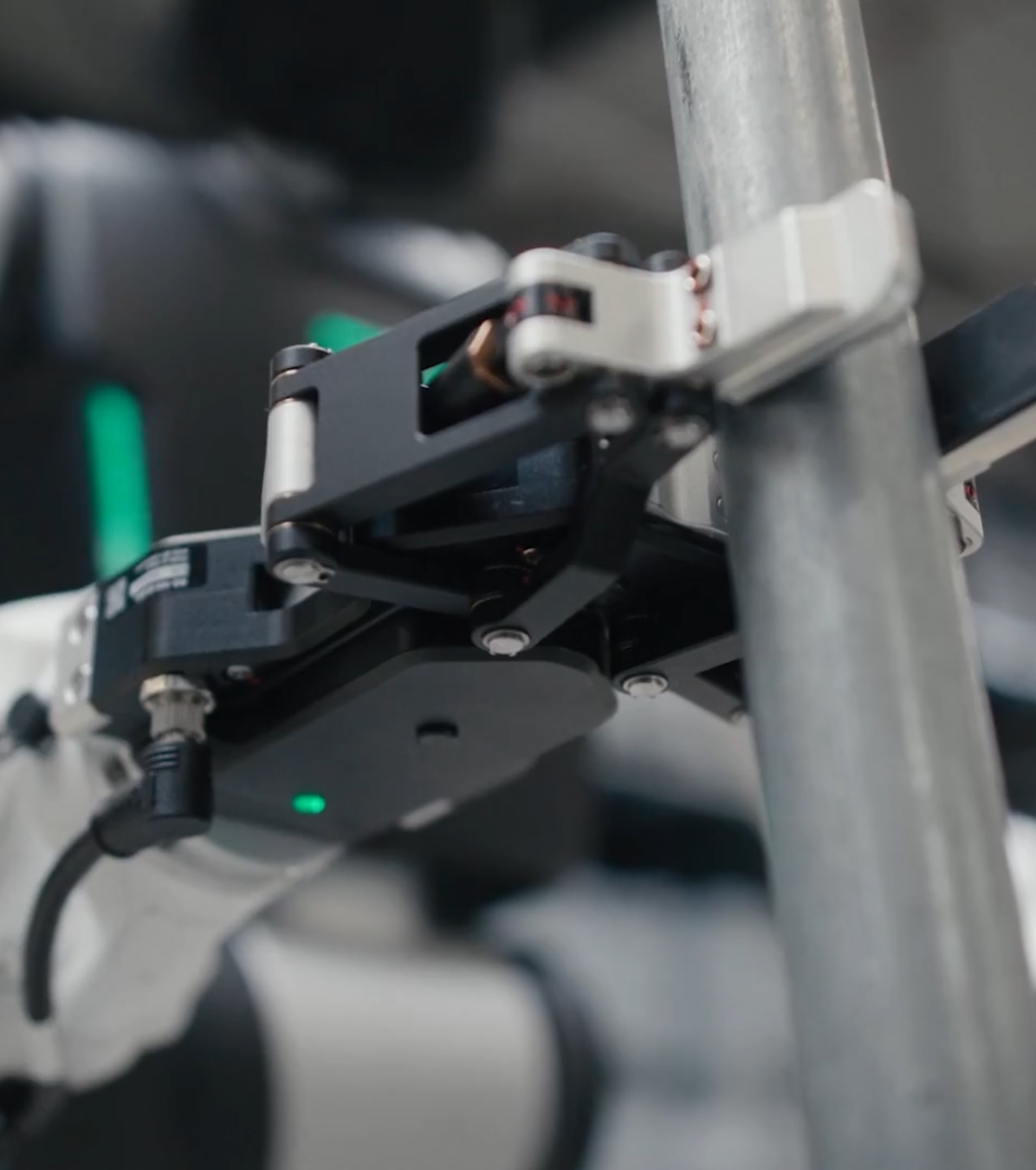 Close-up of a black robotic gripper with a green status light clamped around a steel handlebar